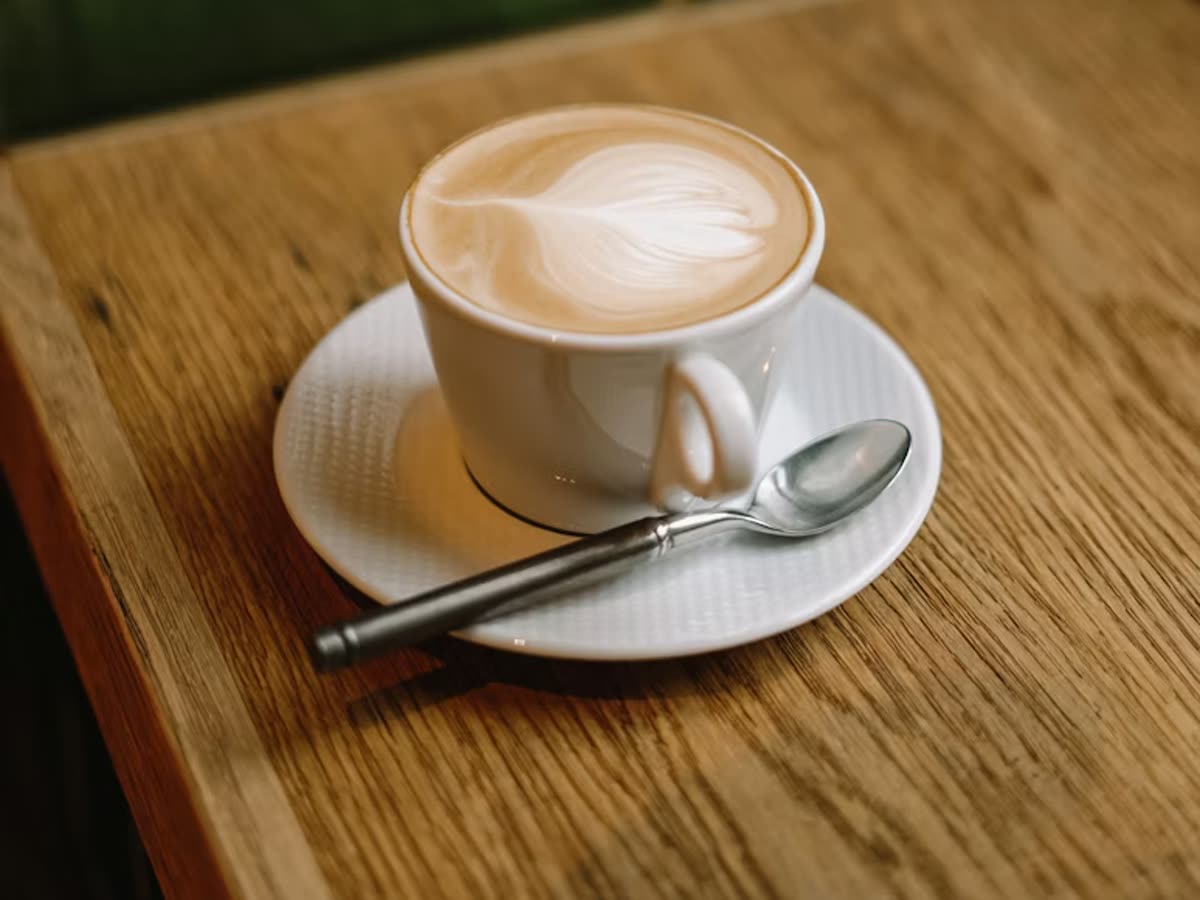 A latte with heart-shaped art on a wooden table against a green-tiled wall
